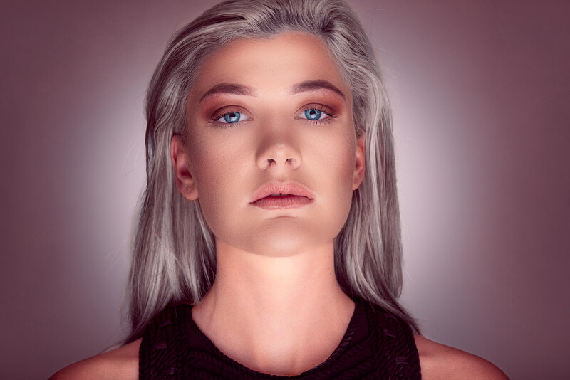 Portrait of a person with long gray hair and pink-toned eyeshadow against a gradient purple background.