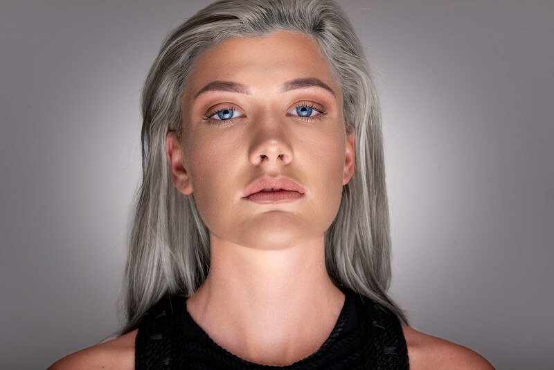 Portrait of a person with long gray hair and blue eyes against a neutral gray background.