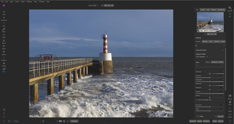 Striped lighthouse on a concrete pier extending into rough ocean waves under a blue sky.