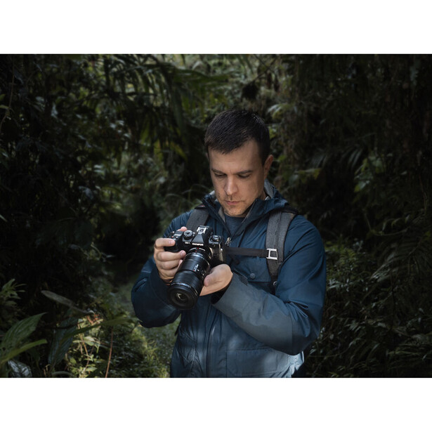 Photographer holding a vintage film camera in a dense forest with green foliage surrounding him.