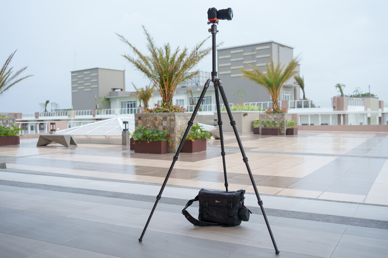 Professional camera on tripod with monopod mounted on rooftop terrace overlooking residential buildings.