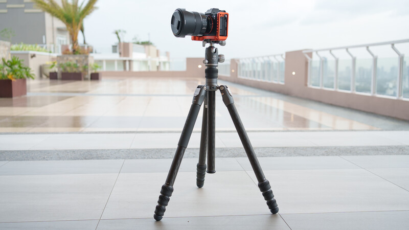 Mirrorless camera mounted on tripod with red rig plate on rooftop terrace overlooking city.