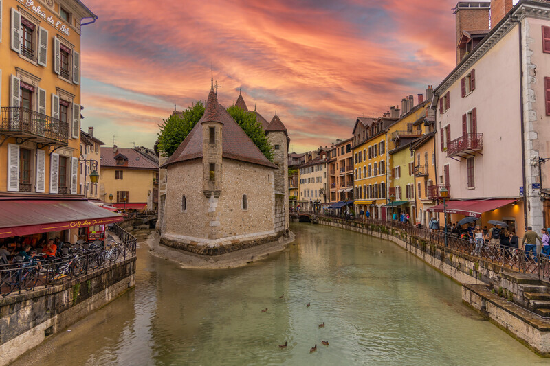 Medieval chapel surrounded by colorful buildings along a waterway during golden hour sunset.