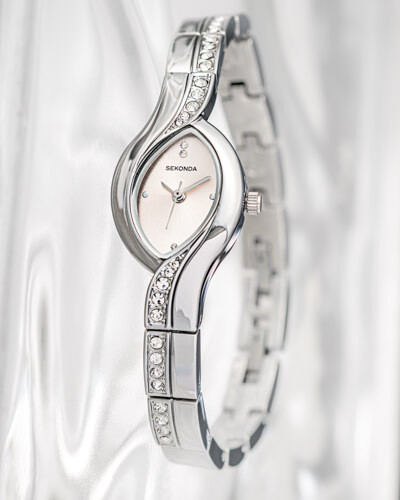Silver-toned bangle watch with oval face and crystal-embellished band against white fabric backdrop.