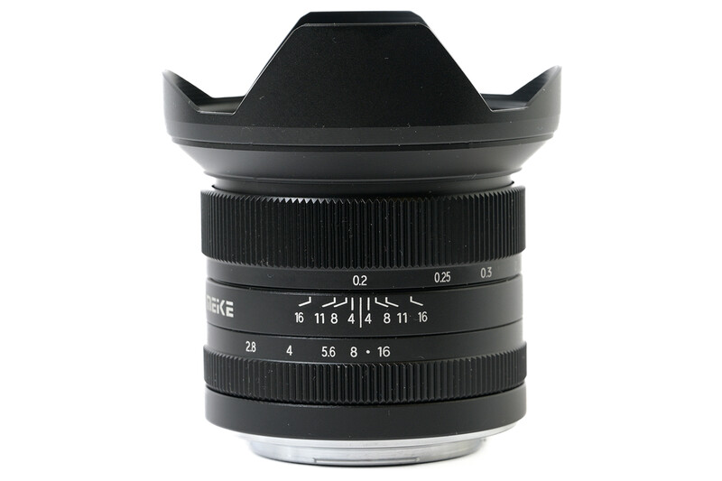 Wide-angle prime lens with black barrel, aperture markings, and lens hood mounted on white background.