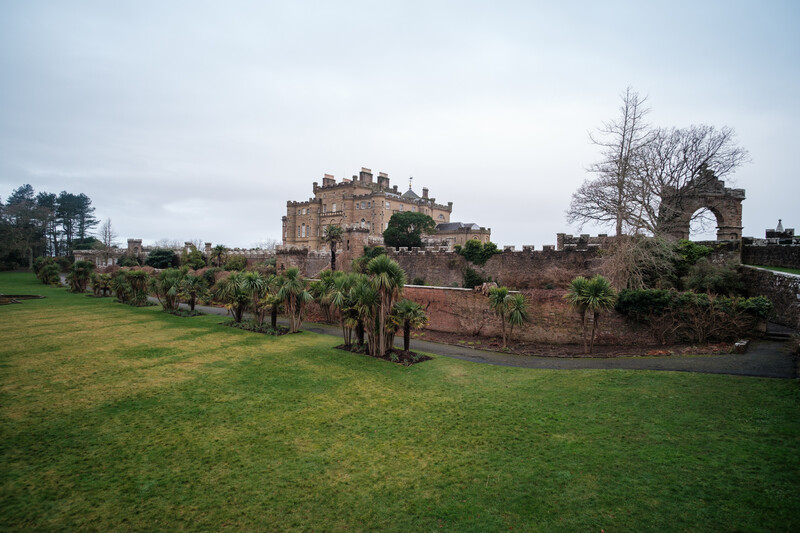 Medieval stone castle on elevated grounds surrounded by manicured lawns and specimen trees.