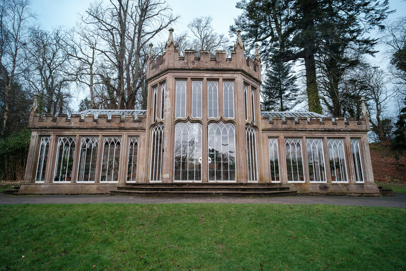 Gothic Revival brick structure with crenellated towers and tall arched windows, surrounded by bare trees and manicured lawn.