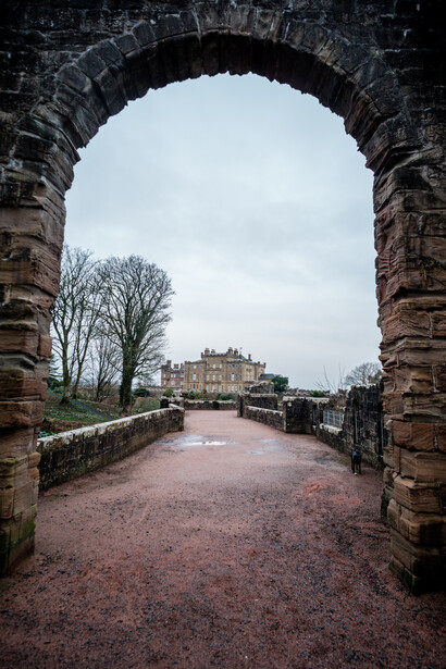 Stone archway framing a distant castle and grounds on an overcast day.