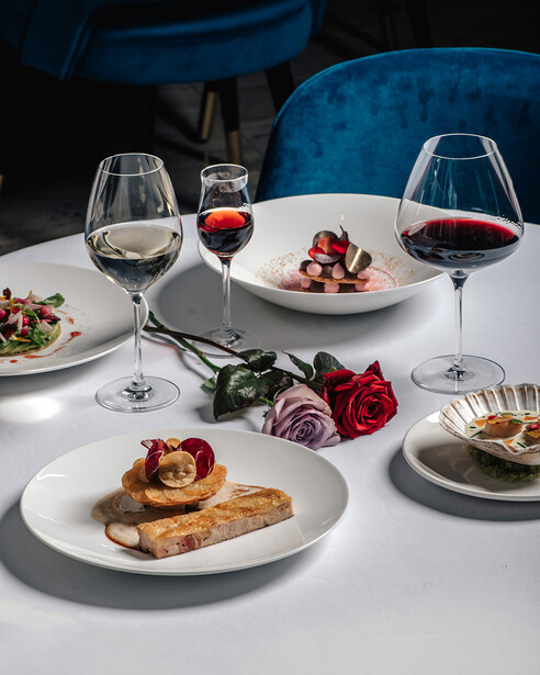 Fine dining table setting with plated dishes, wine glasses, and fresh roses under professional studio lighting.