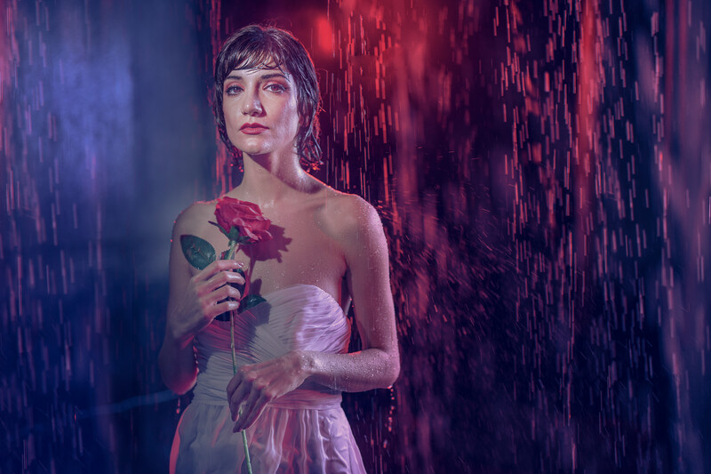 Woman in sheer dress holding a red rose in dramatic blue and red lighting.