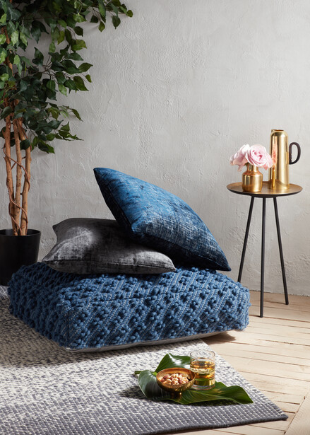 Blue textured armchair with matching pillows in a minimalist interior space.