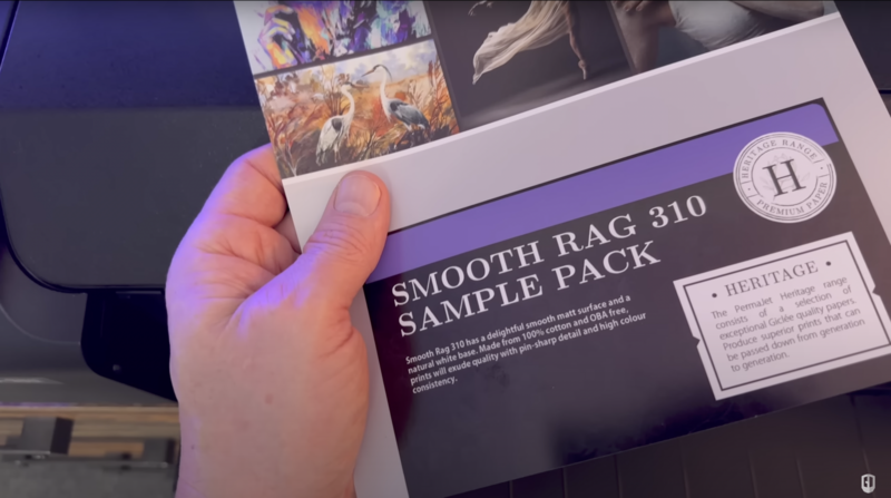 Hand holding a Heritage Smooth Rag 310 Sample Pack box with purple accent lighting.