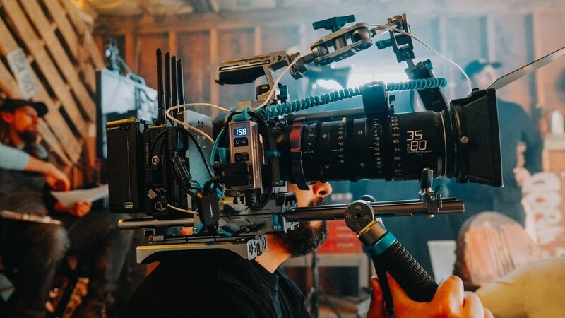 Professional cinema camera mounted on rig with follow focus system and wireless controls against urban backdrop.