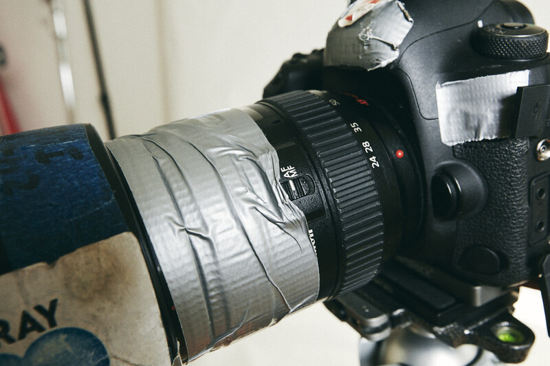 DSLR camera with telephoto lens attached, held at an angle against a light background.