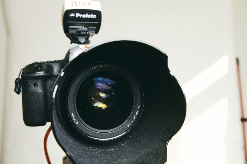 Canon DSLR camera with attached Profoto flash and lens hood, viewed from above against white background.