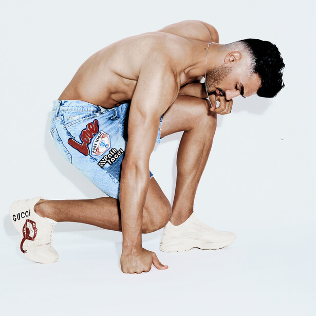 Shirtless man in crouched pose wearing light blue shorts against white background.