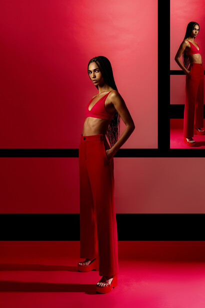 Woman in red crop top and high-waisted pants posing against geometric red and black wall.