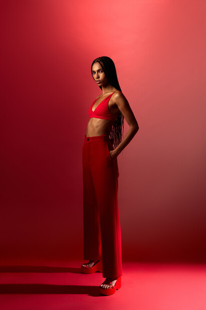 Woman in red crop top and high-waisted pants against monochromatic red background.