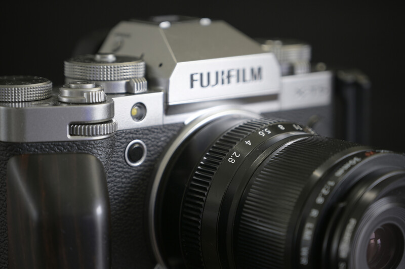 Fujifilm mirrorless camera with attached telephoto lens against dark background.