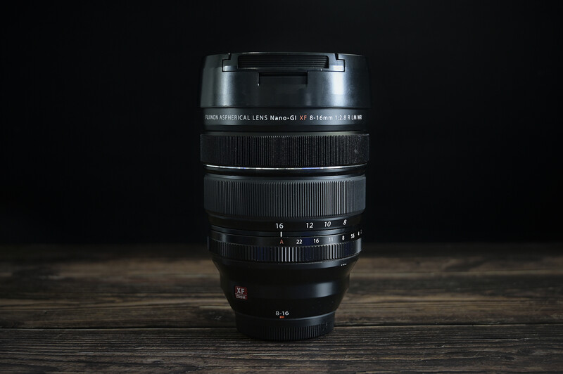 Black telephoto zoom lens mounted vertically against dark background on wooden surface.