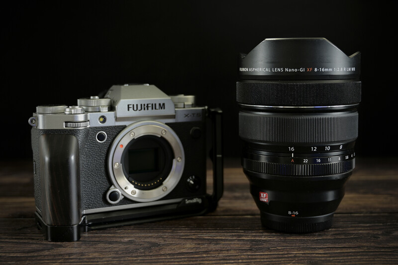 Fujifilm GFX medium format camera body next to a large telephoto zoom lens on wooden surface.