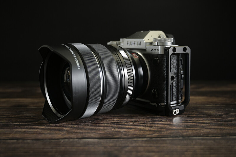 Fujifilm mirrorless camera with wide-angle lens and lens hood on wooden surface against dark background.