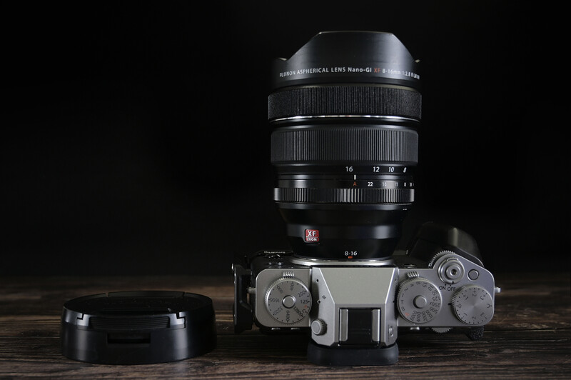 Vintage rangefinder camera with attached telephoto lens and lens cap on wooden surface.