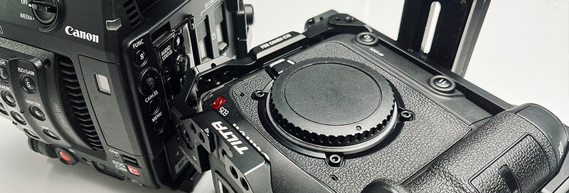Professional cinema cameras displayed on white surface, showing Canon and other broadcast video equipment body and controls.