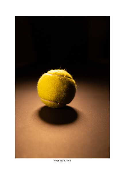 Yellow sphere with textured surface casting a dark shadow on warm brown ground against black background.