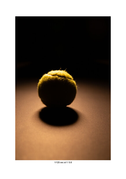Golden sphere with bright rim lighting against dark background and warm tan surface.