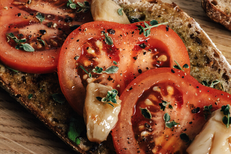 Sliced tomatoes and melted cheese on toasted whole grain bread with fresh herbs and cracked pepper.
