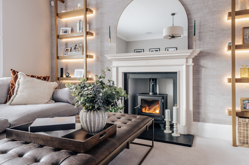 Modern living room with fireplace, lit shelving, arched mirror, and styled coffee table with plant arrangement.