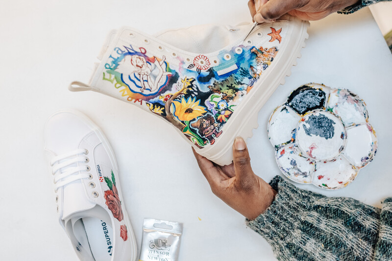 Flat lay of white sneaker, patterned tote bag, and decorative hat arranged on white surface.