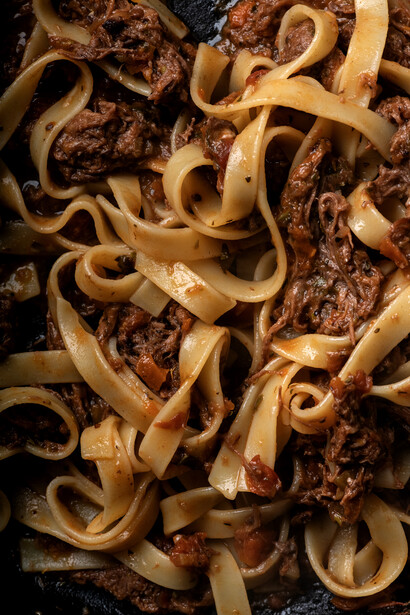 Egg noodles tossed with ground beef in a dark sauce on a black plate.