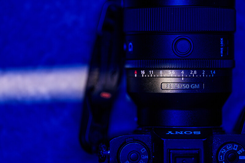 Sony camera with telephoto lens mounted on tripod against blue-tinted background with light streaks.