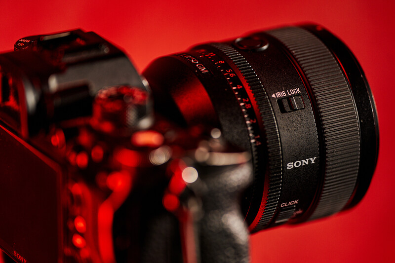 Sony lens mounted on a camera body against a red background with studio lighting.