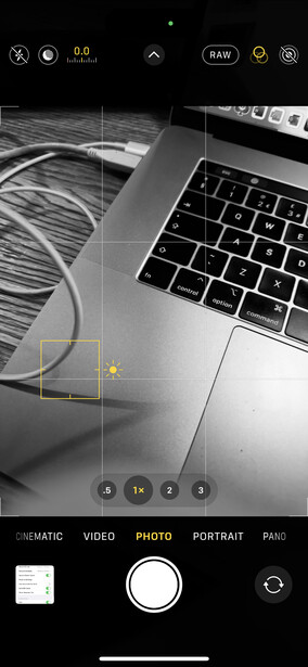 Screenshot of a mobile camera app displaying a laptop and cables with grid overlay and editing controls.
