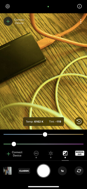 Screenshot of mobile photo editing app showing flat lay composition with cables and tablet on wooden surface.