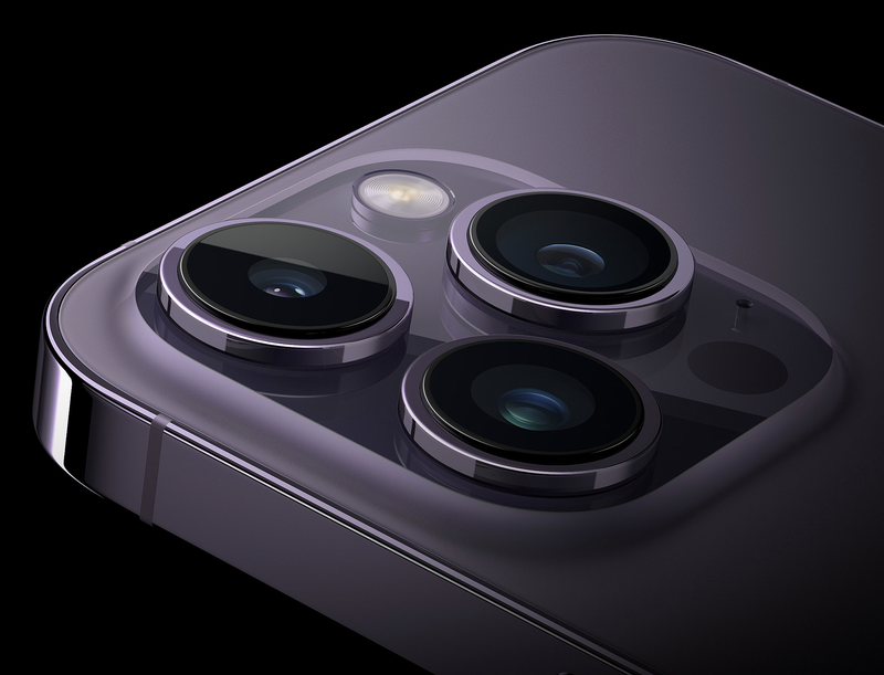 Close-up of a smartphone's rear camera module with three lenses and flash arranged on a dark purple surface.