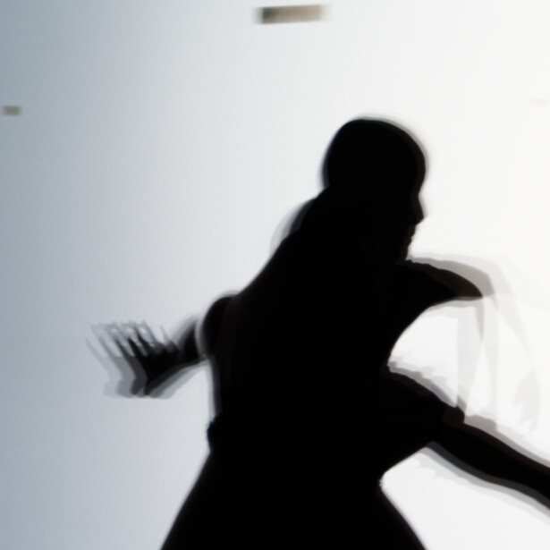 Silhouette of a person in dynamic pose against bright backlit background.