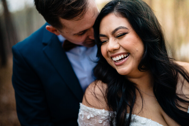 Man in blue blazer and light blue shirt kissing woman's cheek while she smiles at camera.
