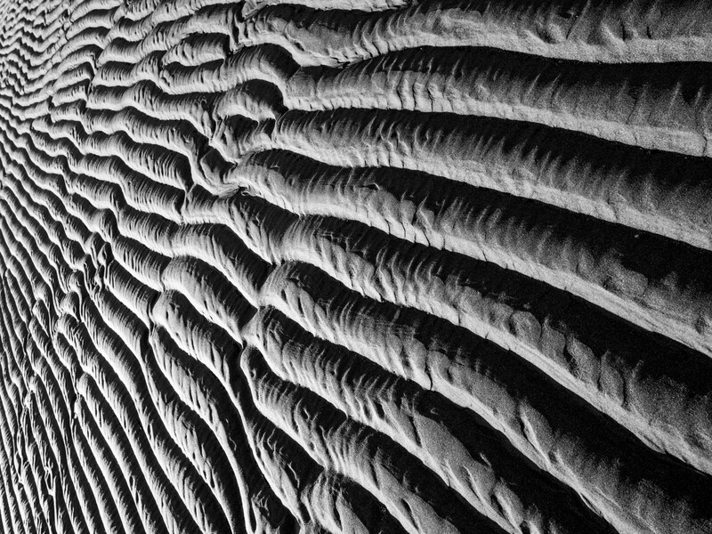 Dramatic black and white close-up of parallel ridged textures creating a flowing, wave-like pattern with deep shadows.