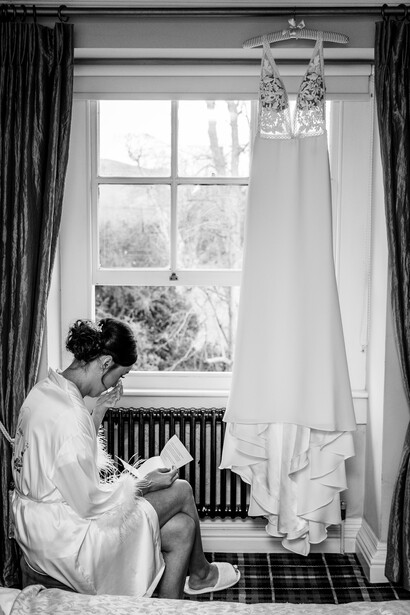 Woman in white dress sitting by window with sheer curtains and pendant light fixture.