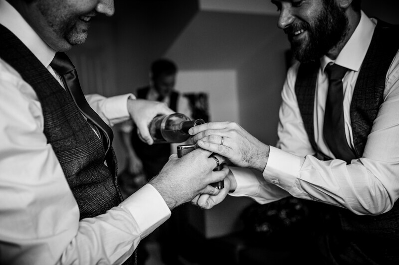Two men in formal attire exchanging a bottle during an indoor celebration.