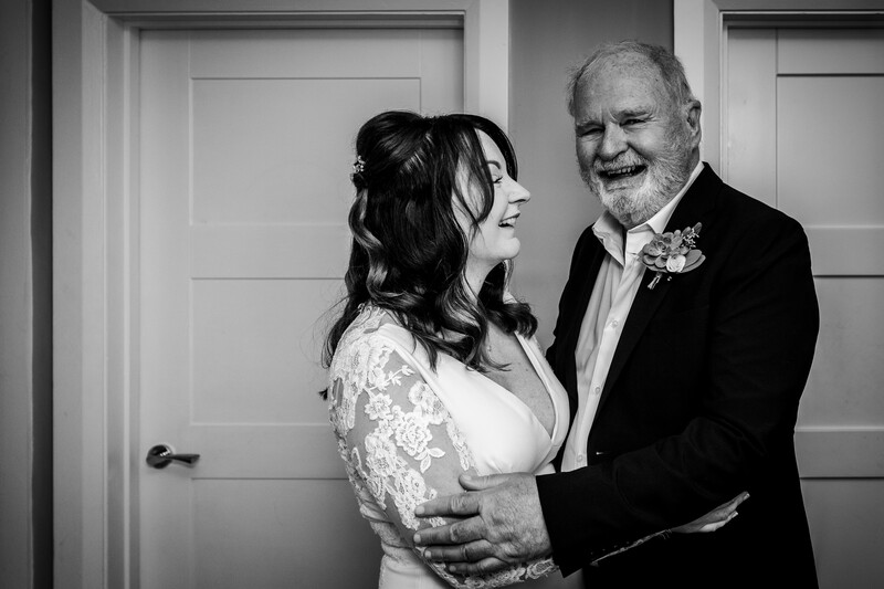 Couple in formal attire embracing and smiling in an indoor setting with white paneled doors.