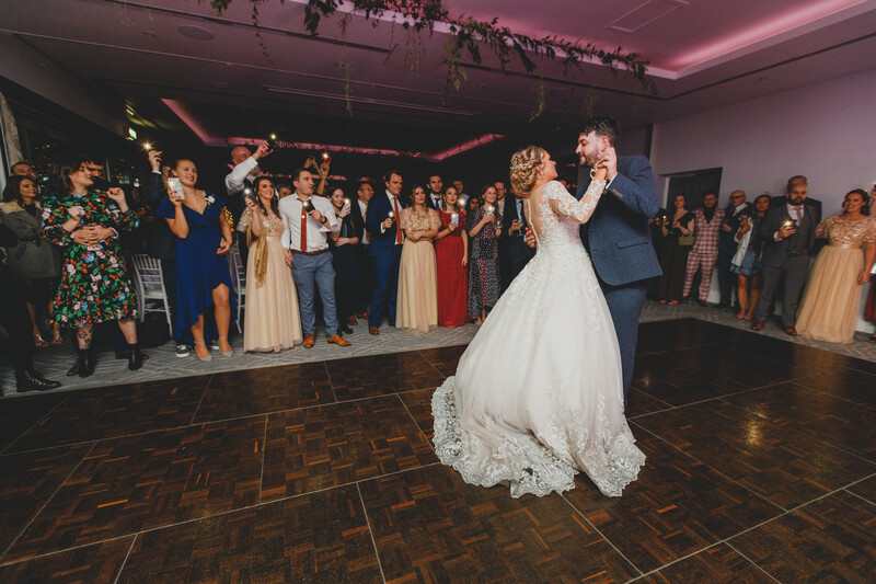 Bride and groom dancing at their first dance during a wedding reception with guests watching.