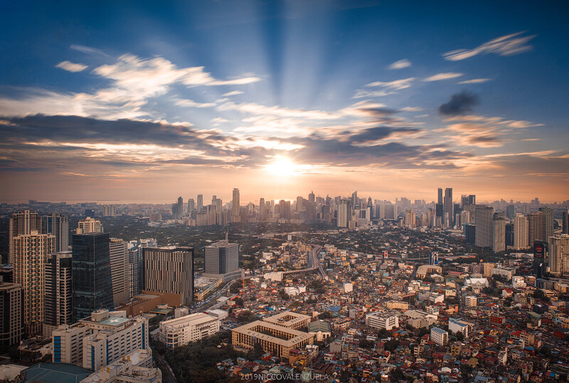 Cityscape at sunset with dramatic clouds and sun rays over downtown skyline and residential neighborhoods.