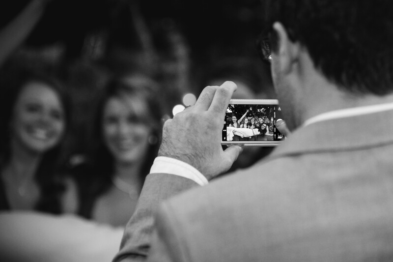 Man holding smartphone capturing photo of two smiling women in black and white.