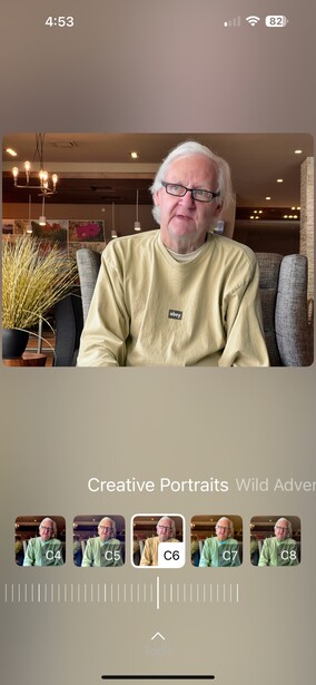 Portrait of an older man wearing glasses and a yellow-green shirt, seated indoors with warm lighting.