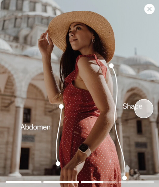 Woman in red polka dot dress wearing wide-brimmed straw hat against historic stone architecture.